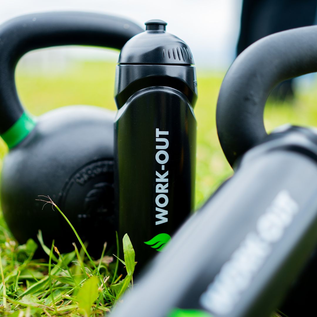 Work-Out herbruikbare zwarte sportbidon met logo, liggend op gras, tussen een kettlebell