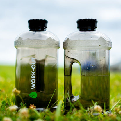 2 Work-Out herbruikbare zwarte drinkbussen van 2 liter met logo, staand in het groene gras